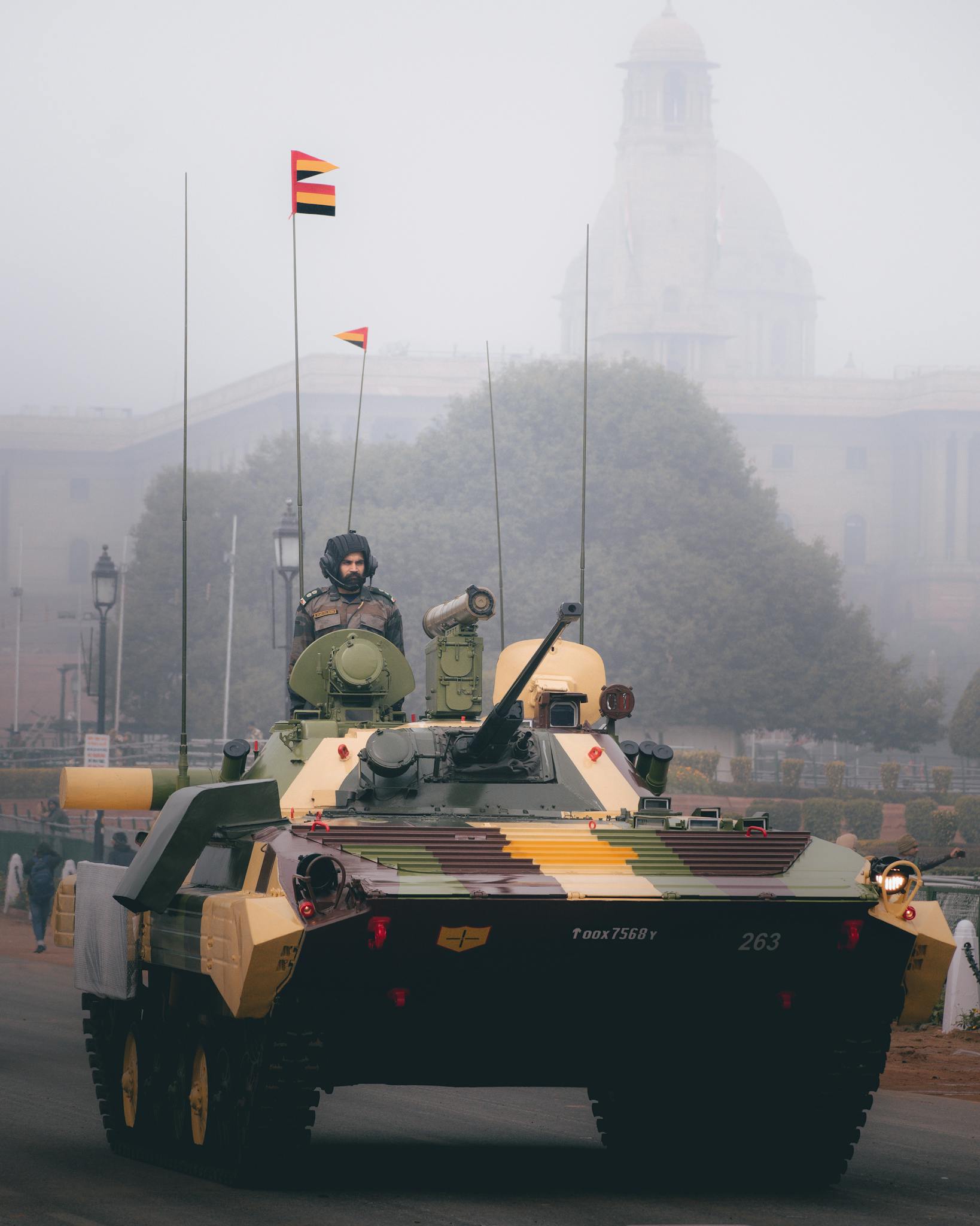 A military parade featuring a camouflaged armored vehicle moving through a foggy landscape.