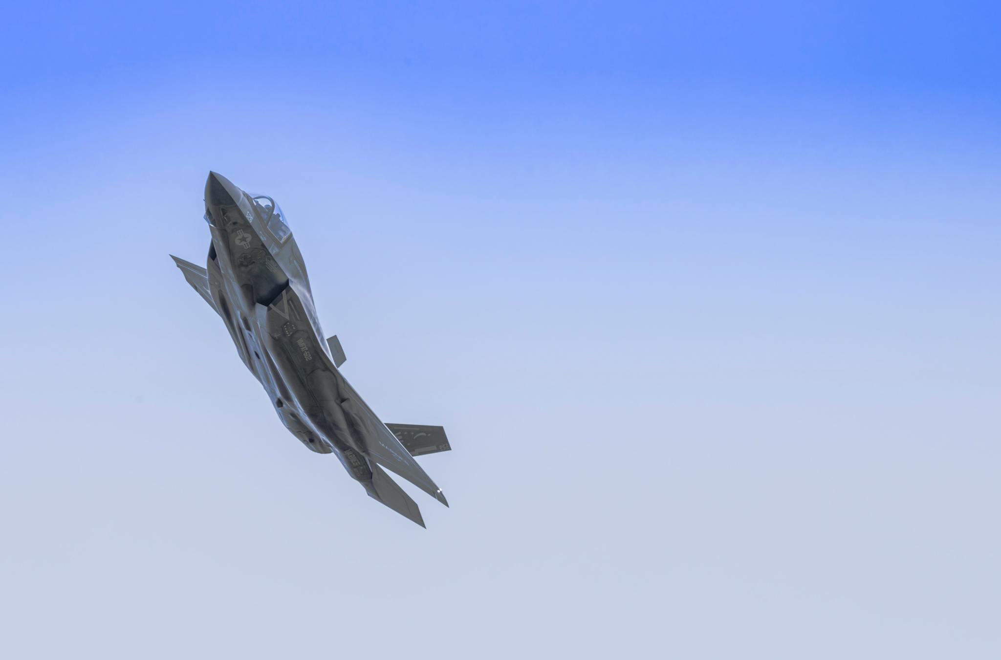 An F-35 fighter jet ascends against a clear blue sky, showcasing advanced aerodynamics.